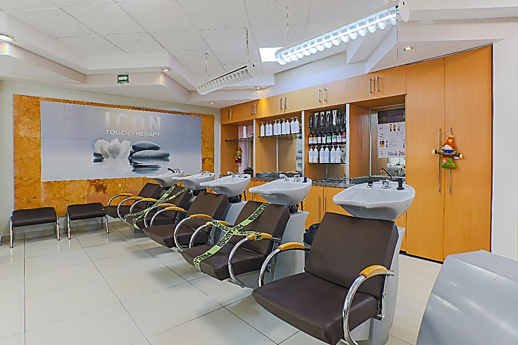 Zona de lavado con cinco sillones café y lavacabezas blancos frente a un mueble de madera con productos