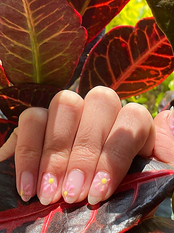 Uñas en rosa claro con florecitas pintadas, sobre hojas rojas